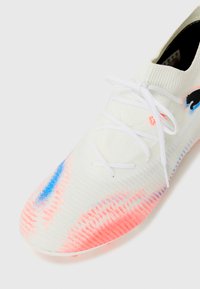 Weißer Sportschuh mit einer strukturierten Oberseite, versehen mit blauen und rosa Farbverlauf-Akzenten, weißen Schnürsenkeln und einem schwarzen Logo an der Seite.