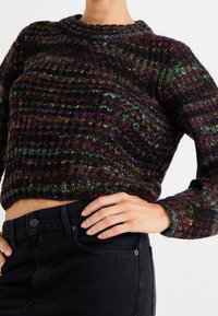 Chunky knit sweater in multi-colored yarn with a dark base, featuring a crew neckline and ribbed texture. Cropped fit, worn with black jeans.