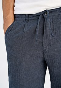 Granatowe spodnie w jodełkę wykonane z teksturowanej tkaniny, z elastycznym paskiem ze sznurkiem oraz bocznymi kieszeniami.