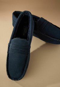 Mocasini din suede albastru închis, cu o căptușeală interioară moale, având accente de cusătură și un design în stil mocasin.