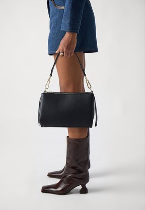 Sac à main en cuir noir avec une finition texturée, doté d'une bandoulière amovible et de quincaillerie dorée. Porté avec des bottes à talons marron.