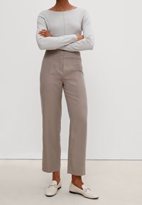 Haut à manches longues gris clair avec un design en V texturé, associé à un pantalon large beige. Des mocassins blancs complètent la tenue.