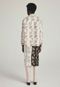 Wit en rode bloemenpatroon jas, gecombineerd met een zwarte en bloemenrok; beige laarzen tot de knie; lange mouwen en een ontspannen pasvorm.