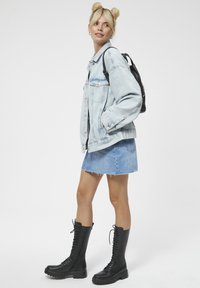 Jasnoniebieska dżinsowa kurtka o luźnym kroju, w połączeniu z jasnoniebieską dżinsową spódnicą. Czarne wysokie botki na sznurowadła, czarna plecak.