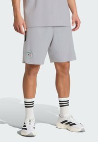 Szare sportowe szorty z naszywką z logo, wyposażone w boczne kieszenie, zestawione z białymi skarpetkami z czarnymi paskami, noszone z białymi butami sportowymi.