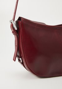 Bordeaux læder skuldertaske med en glat tekstur, rund form og sølv hardware detaljer. Har et quiltet design og justerbar rem.