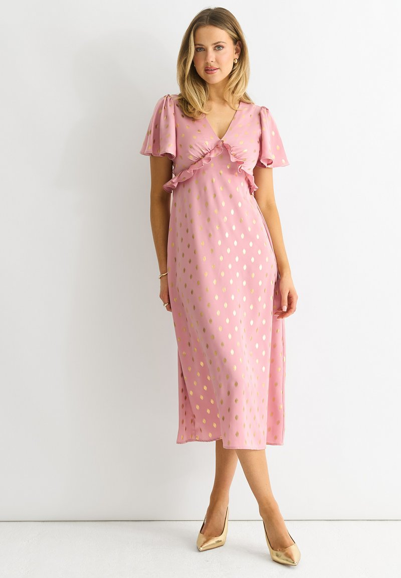 Pink floral dress featuring short ruffled sleeves, a wrap design, and gold polka dots. Complemented by gold pointed-toe heels.
