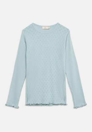 Lyseblå langermet skjorte med lite diamantformet hullmønster, rund halslinning og rynkede kanter på mansjetter og kant.