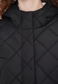 Μαύρο καπιτονέ μπουφάν με ψηλό γιακά και κουκούλα, με διαμάντι σχέδιο και λεία υφή. Χωρίς ορατά μεταλλικά εξαρτήματα ή διακοσμητικά στοιχεία.