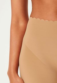 Beige high-waisted shorts met een gegolfde bovenrand, gemaakt van een gladde, rekbare stof die een naadloze uitstraling geeft.