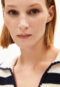 Stickad tröja med horisontella marinblå och krämfärgade ränder, med en texturerad väv och V-ringning. Modellen har kort hår och minimal sminkning.