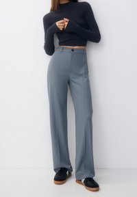 Aangesloten marineblauwe geribbelde trui, hoog-waist lichtgrijze broek en zwarte sneakers met witte strepen. Tailored ontwerp met een soepele textuur.