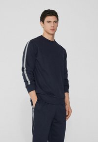 Marineblauer Sweatshirt mit Rundhalsausschnitt und langen Ärmeln, ausgestattet mit grauen Streifen an den Ärmeln. Hergestellt aus einem strukturierten Baumwollmischgewebe.