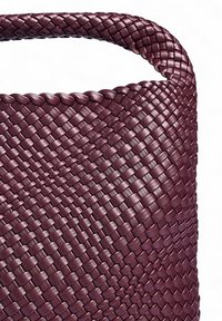 Vävd handväska i djup bordeauxläder med en strukturerad form och slät yta; har ett runt handtag och en intrikat flätad mönster.