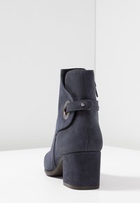 Botín de cuero azul marino con punta redonda, superficie texturizada y un acento metálico redondo en la correa. Tacón apilado.