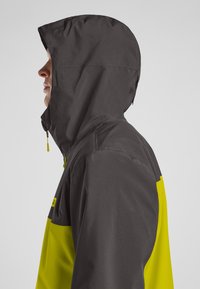 Wasserabweisende Jacke in Schwarz und leuchtendem Gelb, ausgestattet mit Kapuze, Reißverschlüssen und glatter Textur, entworfen für den Einsatz im Freien.