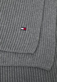 Grå strikket sweater med ribbet tekstur. Har en lille rød, hvid og blå logo-patch på venstre forsiden.