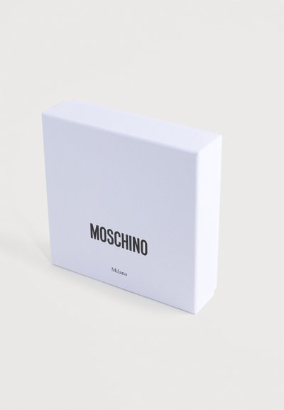 Λευκό χαρτόκουτο με ομαλή υφή. Στην πρόσοψη εμφανίζεται η λέξη «MOSCHINO» με έντονα μαύρα γράμματα, στο κέντρο πάνω από τη λέξη «Milano» με μικρότερα γράμματα.