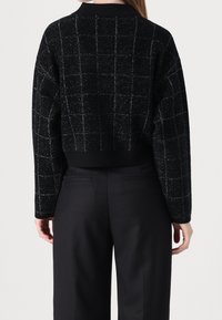 Maglione cropped nero con un motivo plaids testurizzato. Presenta un collo a costine e maniche lunghe. Abbinato a pantaloni neri.