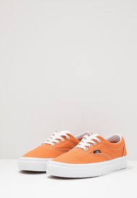 Baskets en toile orange avec des lacets blancs, semelles en caoutchouc blanches et un design simple. Détails de couture remarquables sur les côtés supérieurs.