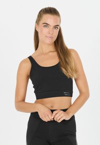 Musta urheilullinen crop top, jossa on pyöreä kaula-aukko, sileä pinta ja koristeellinen ommel helmoissa. Yhdistetty mustiin legginsseihin.