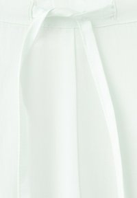 Gros plan d'un tissu blanc avec une couture visible et un cordon plat noué au centre en haut.