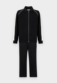 Μαύρη φόρμα με λευκές ρίγες στα πλαϊνά, μπουφάν με φερμουάρ μέχρι κάτω και γιακά, και παντελόνι ίσιας γραμμής σε μονόχρωμο φόντο.