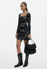 Sort blomsteret mini kjole med lange ærmer og firkantet halsudskæring; parret med sorte cowboystøvler med intrikate syninger og en struktureret sort håndtaske.