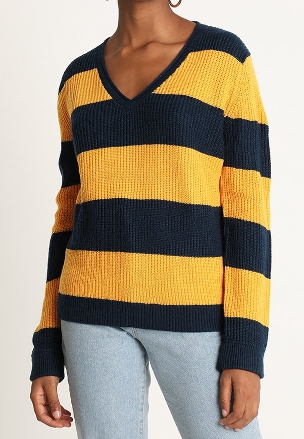 Pull à col en V et manches longues avec de larges rayures horizontales bleu marine et jaune moutarde porté avec un jean bleu clair.