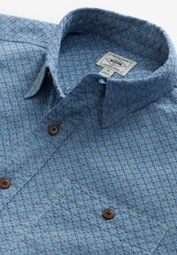Blaue gemusterte Hemd mit Knöpfen aus strukturiertem Stoff, das ein kleines geometrisches Design aufweist, zwei braune Knöpfe und einen klassischen Kragen hat.