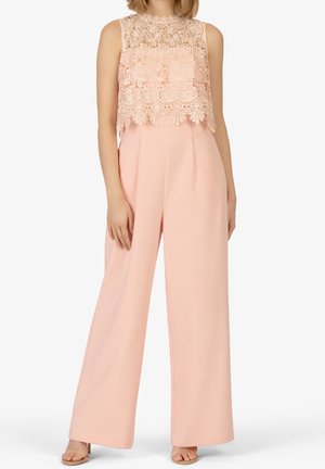 Vrouw draagt een mouwloze blush roze kanten crop top gecombineerd met hoge taille wijde pijpen broek en nude open teen hakken.