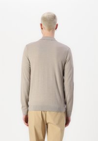 Ανοιχτό μπεζ μακρυμάνικο πουλόβερ με κλασικό γιακά, ribbed μανσέτες και στρίφωμα, με λεία υφή και διακριτές ραφές.