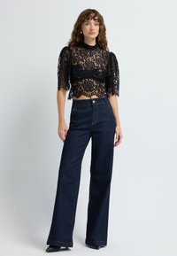 Sort blonde crop top med puffærmer, parret med højtaljede mørk denimbukser. Mørk ensfarvet, bemærkelsesværdig blonde tekstur og detaljer.