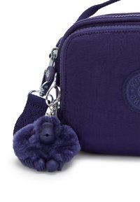 Purple fabric crossbody bag with a soft, plush gorilla charm attached. Features silver hardware and a textured strap. Compact and sleek design.