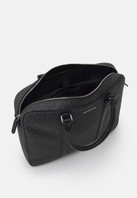 Sac à main noir à motif avec des accents en cuir, fermeture zippée, doubles poignées et compartiment intérieur. Présente le logo de la marque à l'avant.