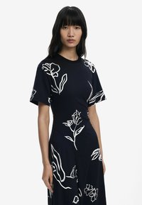 Marineblaues Kleid mit kurzen Ärmeln, verziert mit weißen Blumenmustern. Glatte Textur mit taillierter Silhouette und rundem Ausschnitt.
