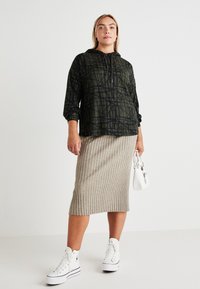 Kapuca temnozelena majica s črnim geometrijskim vzorcem, kombinirana z bež rebrasto midi krilo in belimi visoki superge. Nosila majhno belo torbico.