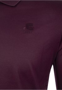 Burgundin värinen polo paita, joka on valmistettu joustavasta kankaasta. Paidassa on hienovarainen Strukturipinta ja painettu logo vasemmassa rinnassa.