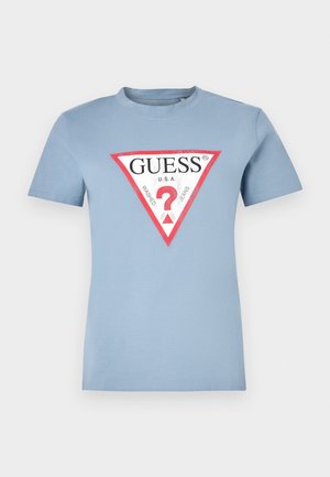 Camiseta de algodón azul claro con mangas cortas y cuello redondo. Presenta un gráfico triangular en rojo y negro con el texto "GUESS U.S.A" y un signo de interrogación.