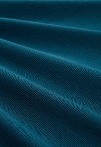 Türkiz textúrájú szövet bordázott mintával, lágy redőkkel és sima felülettel, gazdag, egyenletes színnel jellemezve.