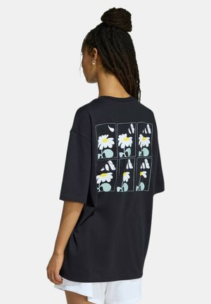 Persona con capelli scuri intrecciati raccolti in uno chignon che indossa una maglietta nera con un design di margherita a sei petali con petali cadenti sulla schiena.