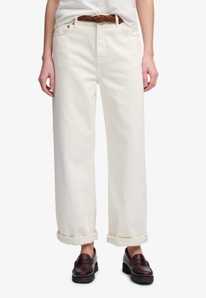 Persona che indossa jeans larghi color avorio risvoltati, cintura intrecciata marrone, camicia bianca infilata e mocassini marrone scuro.