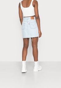 Ljusblå denimkjol med fransar i nederkant, två bakfickor och en brun läderetikett. Bärs med en vit ribbad crop top och vita stövlar.