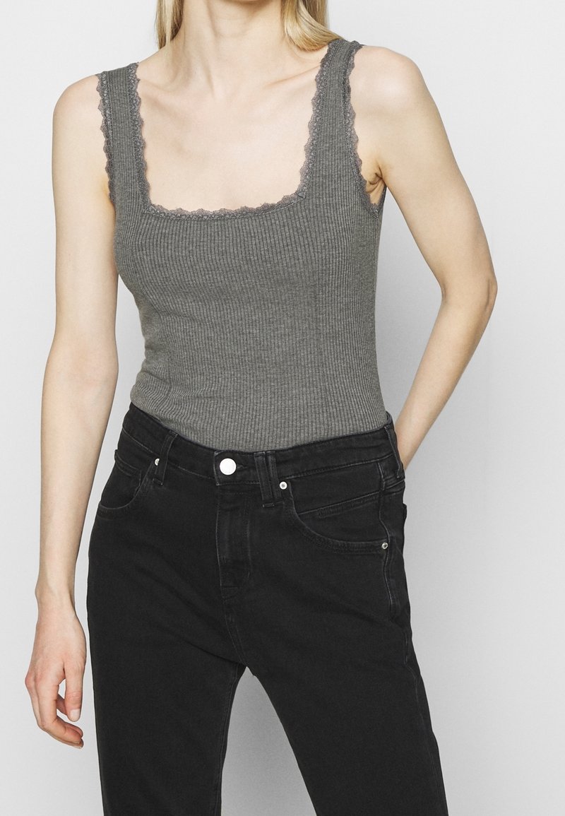 Débardeur gris côtelé avec un col carré et des bordures en dentelle ; porté avec un jean noir taille haute, mettant en valeur une coupe ajustée.