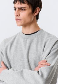 Hellgrauer Pullover mit Rundhalsausschnitt, aus einem weichen, strukturierten Stoff gefertigt. Mit überschnittenen Schultern sowie geripptem Hals- und Bündchenbereich.