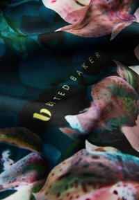 Seidenschal mit einem lebhaften Blumenmuster in Grün-, Rosa- und Blautönen, versehen mit dem goldenen "Ted Baker"-Logo. Weiche Textur.