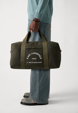 Grüne Nylon-Reisetasche mit doppelten Griffen, weißem bedrucktem Logo, rechteckiger Form und strukturierter Oberfläche. Mit Reißverschlussöffnung an der Oberseite.