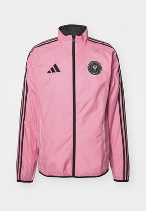 Pink windbreaker jacket with a black zipper, black accents, and three black stripes along the sleeves. Features a circular logo on the chest.
