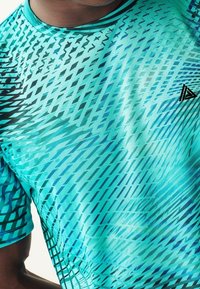 Camiseta deportiva turquesa hecha de tela sintética, con patrones diagonales negros, mangas cortas y cuello redondo.