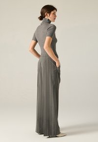 Maglione a collo alto grigio a coste con maniche corte abbinato a pantaloni a gamba larga a righe sottili e vita alta. Texture sottile e silhouette aderente.